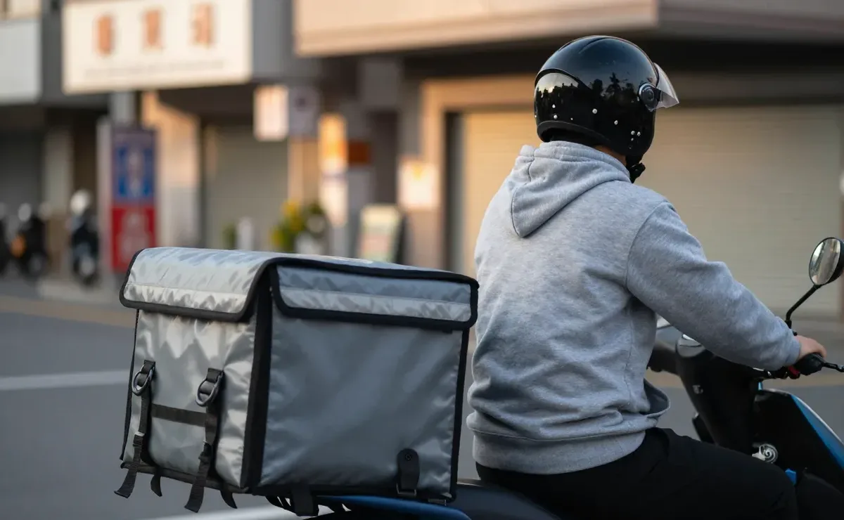 穿灰色帽T的外送員背著保溫箱騎在機車上